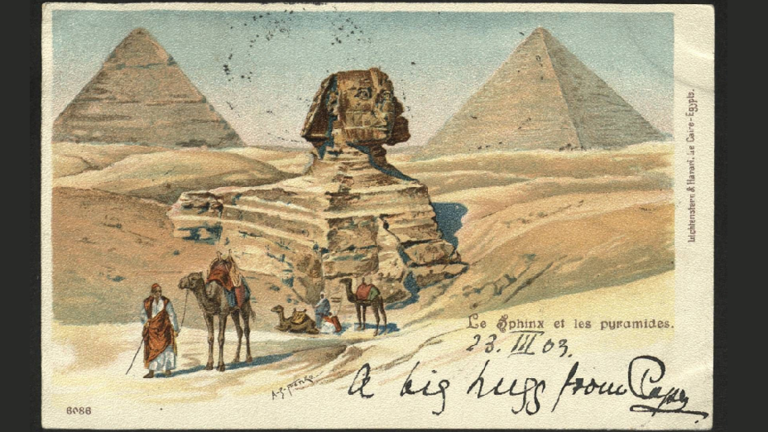 Historische Postkarte: Sphinx, dahinter die Pyramiden, im Vordergrund Ägypter mit Kamelen