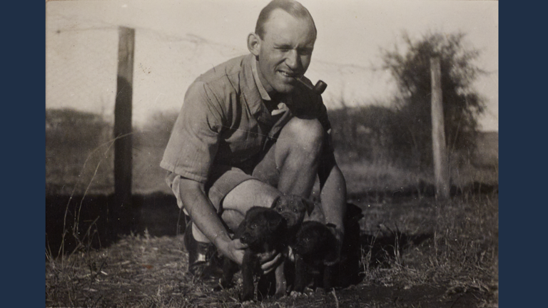 Historisches Foto: Ein Mann hockt auf dem Boden, vor sich drei Hundewelpen