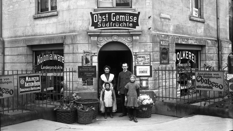 Historisches Foto: Ein Paar mit zwei Kindern steht vor dem Eingang eines Lebensmittelgeschäfts