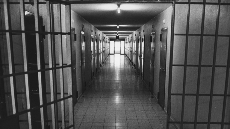 Historisches Foto: Blick in einen Gefängnisflur, vorne geöffnete Gittertür, zu beiden Seiten des Flurs Zellentüren