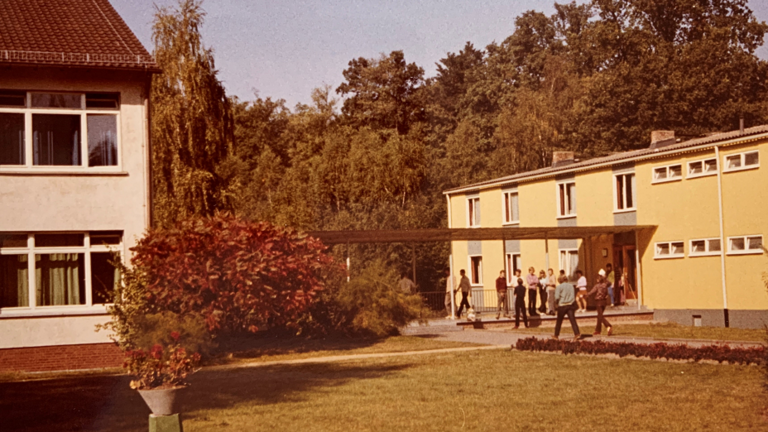 Modernes Foto: Links ein schulähnliches Haus, rechts ein zweistöckiges Wohnhaus, dahinter Bäume