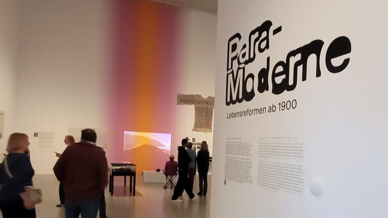 Menschen stehen vor einer weißen Wand mit der Aufschrift Paramoderne