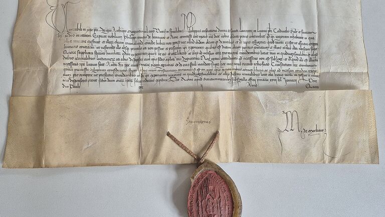 Gefaltetes Pergamentdokument mit handschriftlichem Text; untenmittig hängt ein rotes Wachssiegel an einer Kordel