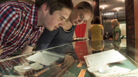 Zwei Mitarbeiter des Landesarchivs betrachten Ausstellungsobjekte in einer Vitrine