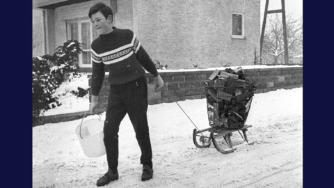 Historisches Foto: Ein Junge zieht einen mit Brennholz beladenen Schlitten durch eine verschneite Wohnstraße, 1956 (HHStAW, 3008/47, 13066)
