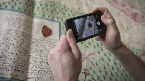 Foto: Zwei Hände, die ein Handy zum Fotografieren über eine Karte halten.