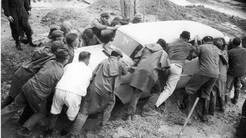 Folgen des Unwetters in Rüdesheim 1966 (HHStAW, 3008/47, 13201) Historisches Foto: Viele Männer versuchen, ein weißes Auto aus dem Schlamm zu schieben.