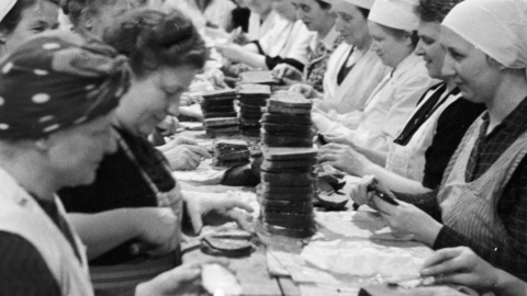 Schwarz-Weiß-Foto: Frauen sitzen einander gegenüber am Tisch und streichen Butterbrote