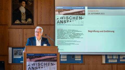 Dr. Johannes Kistenich-Zerfaß, Ltd. Archivdirektor des Hessischen Staatsarchivs Marburg Modernes Foto: Mann steht am Rednerpult, hinter ihm rechts eine Präsentationsleinwand