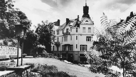 Historisches Foto: Grünanlage, im Hintergrund ein Wohnhaus