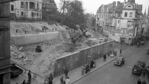 Historisches Foto: Grundmauern, darin Baugeräte, im Hintergrund Wohnhäuser