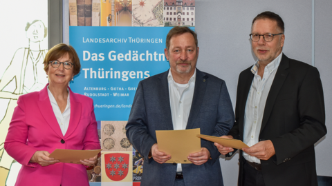 Dr. Sabine Graf, Thomas Wagner, Prof. Dr. Andreas Hedwig Modernes Foto: Eine Frau und zwei Männer halten Dokumentenmappen in den Händen