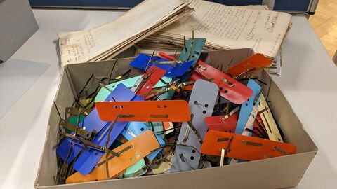 In der alltäglichen Archivarbeit fällt manchmal viel Metall an. Modernes Foto: Karton mit Heftklammern, dahinter frühneuzeitliche Akten