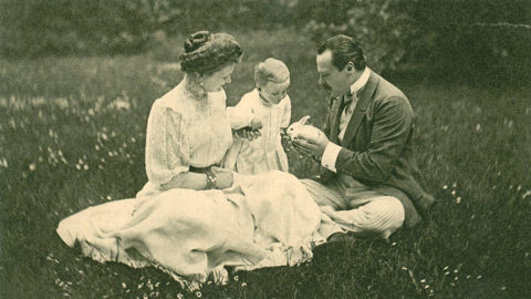 Historisches Foto: Eine Frau, ein Kleinkind und ein Mann sitzen auf einer Wiese, der Mann hält ein weißes Kaninchen in den Händen