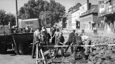 Verlegung des Straßenpflasters in der Rheingaustraße in Biebrich, um 1960 (HHStAW, 3008/47, 12832) Historisches Foto: Männer reichen sich Steinquader zur Pflasterung der Straße
