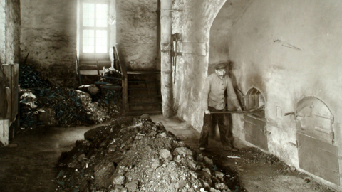 Heizer im Siedehaus 6 in Bad Nauheim, 1910 (HStAD, R 4, 30297/8 UF) Historisches Foto: Blick in einen Heizungsraum, im Vordergrund Kohlehäufen, rechts ein Arbeiter an gemauerten Öfen