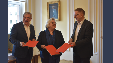 Gute Stimmung nach der Unterzeichnung des Notfallverbundes Wiesbaden Modernes Foto: Zwei gutgelaunte Männer und eine Frau halten rote Mappen in den Händen