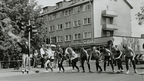 Startschuss zum Stadtstaffellauf Ecke Schwanallee / Leopold-Lucas-Straße in Marburg, 1976 (StadtA MR, S. 3/1, 16) Historisches Foto: Junge Läuferinnen an der Startlinie, am Rand ein Mann mit gerade abgefeuerter Startpistole