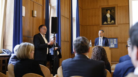 Menschen in einem Vortragsraum, vorne zwei Männer die sprechen