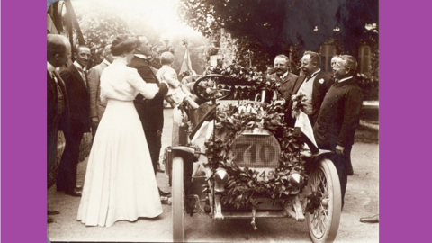 Historisches Foto: Etliche Herren und eine weißgekleidete Dame umringen einen blumengeschmückten Rennwagen