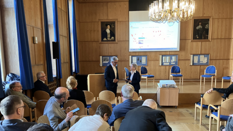 Mann im Anzug übergibt einer Frau eine Plakette