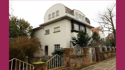 Auffälliges Dach: Das Kleine Glückerthaus auf der Mathildenhöhe, 2025 Foto: Graues Haus mit auffällig tonnenförmigem Dach in einem Vorgarten in einer Wohnsiedlung