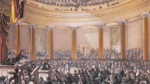 Kolorierter Stahlstich: Blick in einen vollbesetzten, runden Kirchenraum, links ein Redner am Pult, darüber deutusche Fahnen