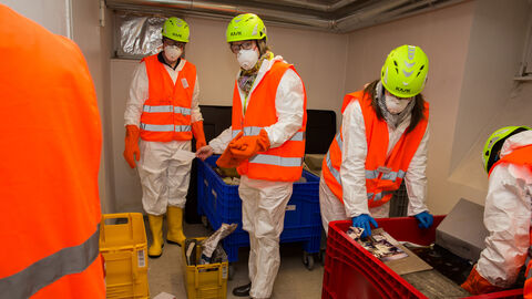 Bei der Bergung muss es schnell gehen. mehrere Personen in orangener Schutzausrüstung mit gelben Helmen retten Unterlagen aus einem Raum