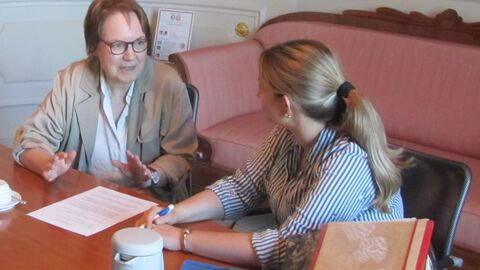zwei Frauen sitzen an einem Tisch und unterhalten sich, vor ihnen liegen Dokumente und Ordner