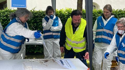 vier Personen in Schutzausrüstung reinigen Unterlagen mit Wasser