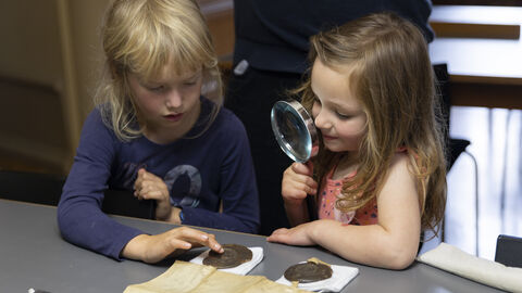 Im Lesesaal lohnt es sich, genauer hinzusehen: Kinder auf Entdeckungsreise im Archiv zwei Kinder vor einer Urkunde, eines hält eine Lupe in der Hand