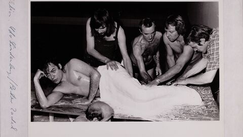 Ein Rockmusiker als Backform: Herstellung einer Gipsform des Sängers Udo Lindenberg im Hamburger Hotel Atlantic, 1979 Foto in schwarz-weiß, ein Mann mit nacktem Oberkörper liegend und von mehreren Menschen ab der Hüfte abwärts eingegipst