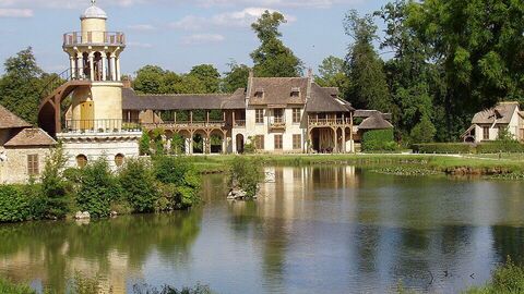 Foto eines Bauernhauses und eines Turms, davor ein kleiner See