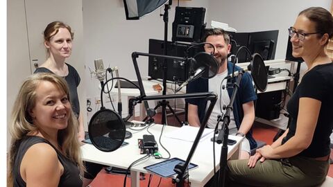 drei Frauen und ein Mann sitzen vor Mikrofonen