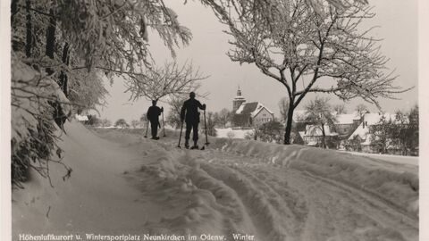 in schwarz-weiß, Foto von zwei Personen in einer tief verschneiten Gegend auf Skiern, Bildunterschrift lautet "Höhenluftkurort u. Wintersportplatz Neunkirchen im Odenw. Winter