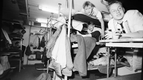 In schwarz-weiß: mehrere Jugendliche liegen auf Etagenbetten in einem engen Raum