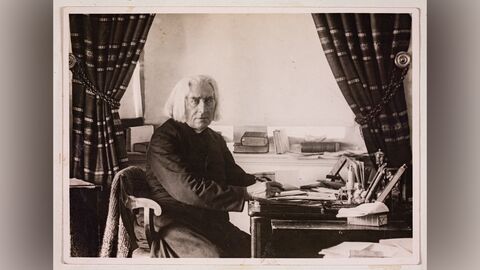 Schwarz-weiß Aufnahme eines älteren Herrn mit längeren weißen Haaren an einem Tisch sitzend