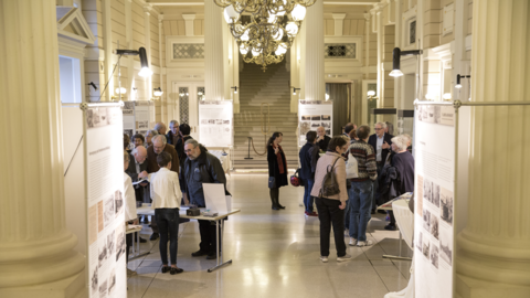 Modernes Foto: Foyer des Staatsarchivs, in dem sich zahlreiche Menschen und Ausstellungstafeln befinden