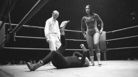 Historisches Foto: Eine Frau liegt am Boden, dahinter steht ein Schiedsrichter. Eine andere Frau steht an ihrem Kopf und blickt auf sie herab.