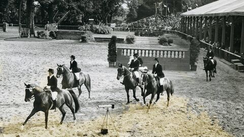 Historisches Foto: Blick in eine Reitparcour, rechts eine überdachte Tribüne, im Vordergrund Reiterinnen