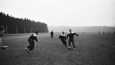 Historisches Foto: Männer in schwarz-weißen Trainingsanzügen trainieren auf einem nebeligen Sportplatz
