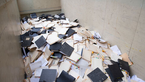 Großer Haufen von Aktenordnern und losen Unterlagen, ungeordnet in einem Container gelagert