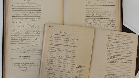 Aufgeschlagenes Registerbuch mit handschriftlich ausgefüllten Formularseiten (Standesamts-Einträge, Seiten 266-267); darüber und daneben lose Dokumente mit weiteren handschriftlichen Angaben zu Personen und Daten.