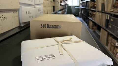 Ein in weißem Papier verpacktes Packet, mit Band umschnürt und der Aufschrift "Praktikantinnen" Nr. 2026 liegt in einem Gang. Dahinter ein Karton mit der Aufschrift "340 Busemann"