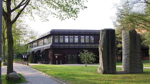 Verwaltungstrakt des Hauptstaatsarchivs: Zweistöckiges Gebäude mit dunkler Blechverkleidung und durchgehender Fensterreihe im Obergeschoss, davor Rasenfläche mit zwei Granitstelen (Kunstwerk)